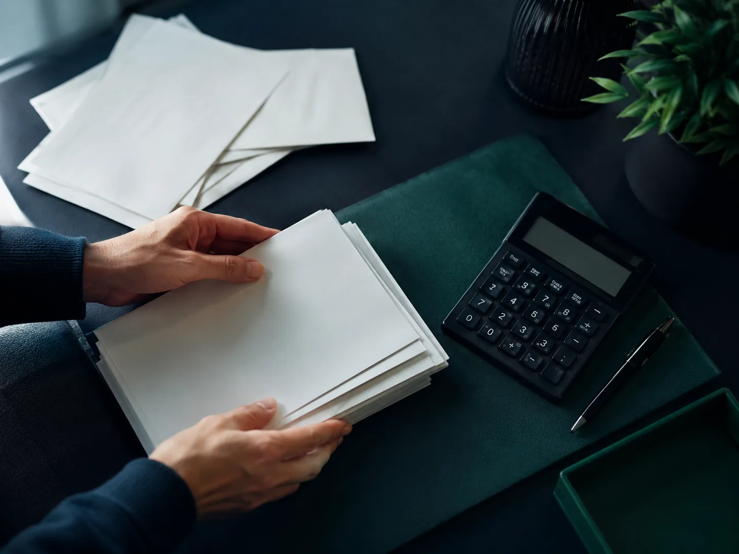 Overhead view of hands stacking several paper statements into one neat pile beside a calculator